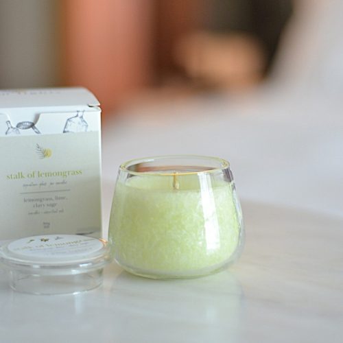 A glass jar candle labeled "Stalk of Lemongrass" with a box and lid beside it, featuring a fresh blend of lemongrass, lime, and clary sage.