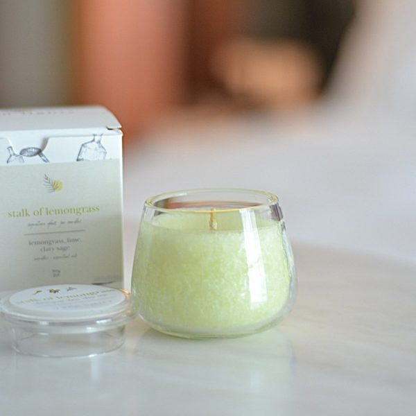 A glass jar candle labeled "Stalk of Lemongrass" with a box and lid beside it, featuring a fresh blend of lemongrass, lime, and clary sage.