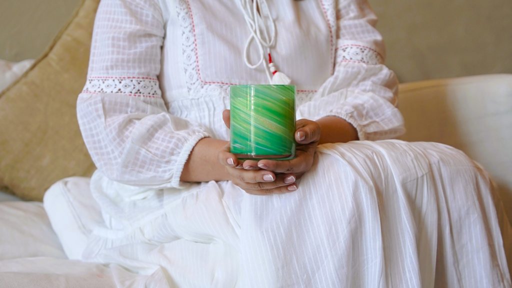 Woman holding a green swirled glass Vata candle from the Palm Lights Ayurveda Candle Collection